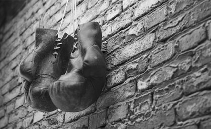 Image: Adobe A black and white image of a pair of old leather boxing gloves hanging against a brick wall