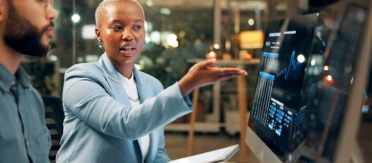 A woman explains information on a computer screen to her colleague.