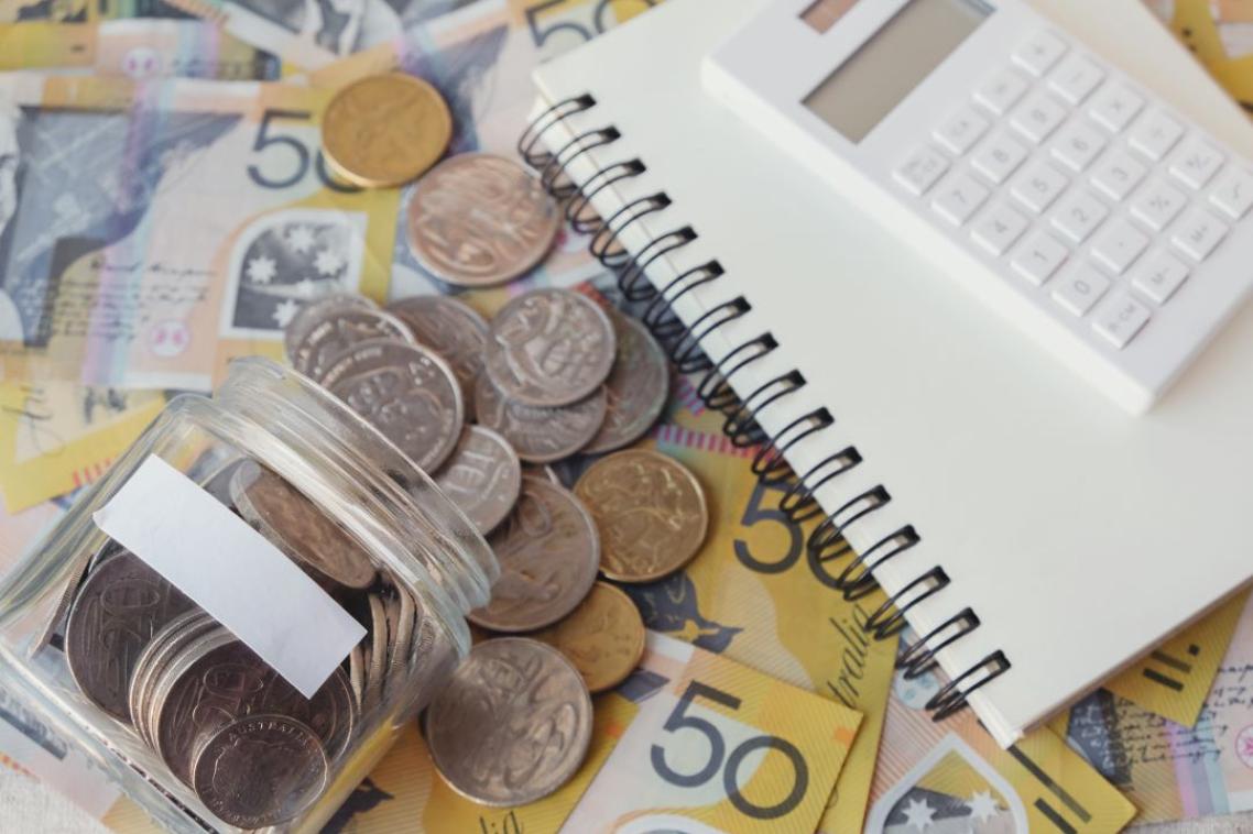 A collection of australian $50 notes, cents, and dollar coins next to a notebook and calculator